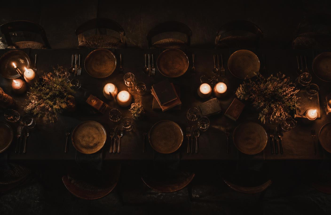 Mesa posta à luz de velas com livros entre os pratos